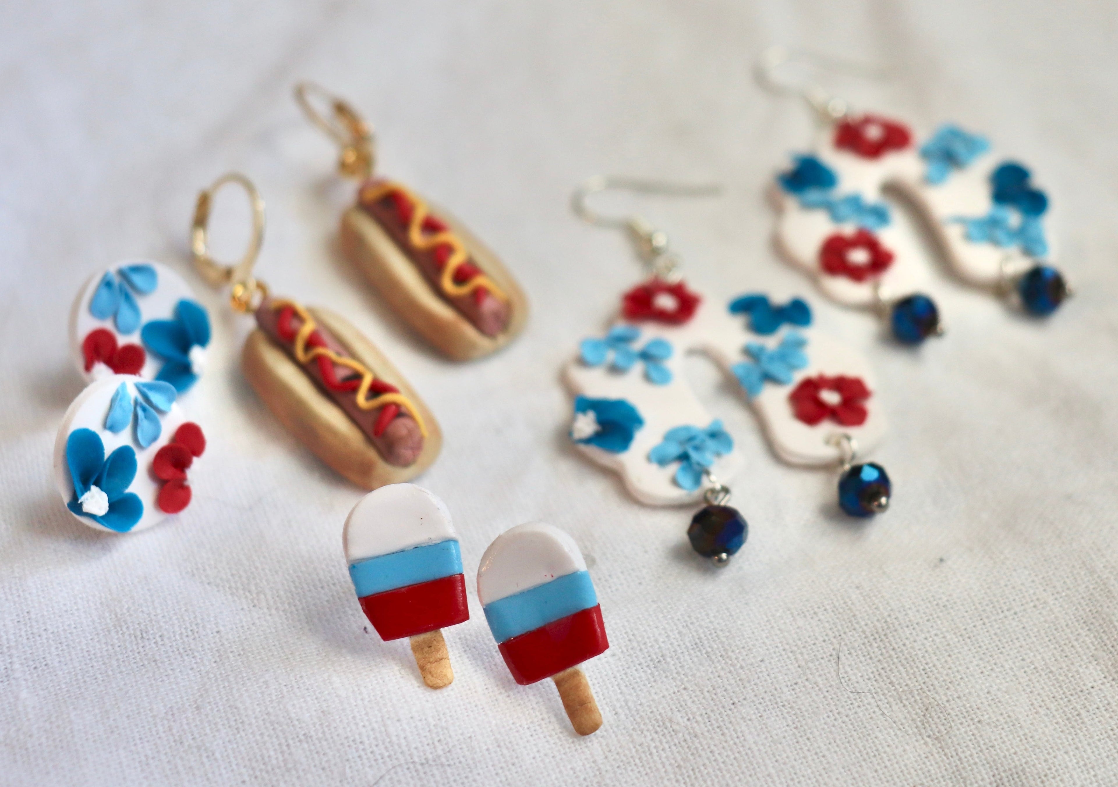 Colorful earrings shaped like hot dogs, ice cream popsicles, and flowers on a white background